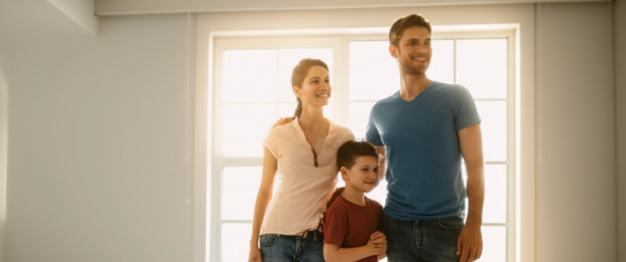 Una familia caucásica feliz sonríe en una habitación luminosa de su nuevo hogar, simbolizando una mudanza exitosa y un nuevo comienzo.